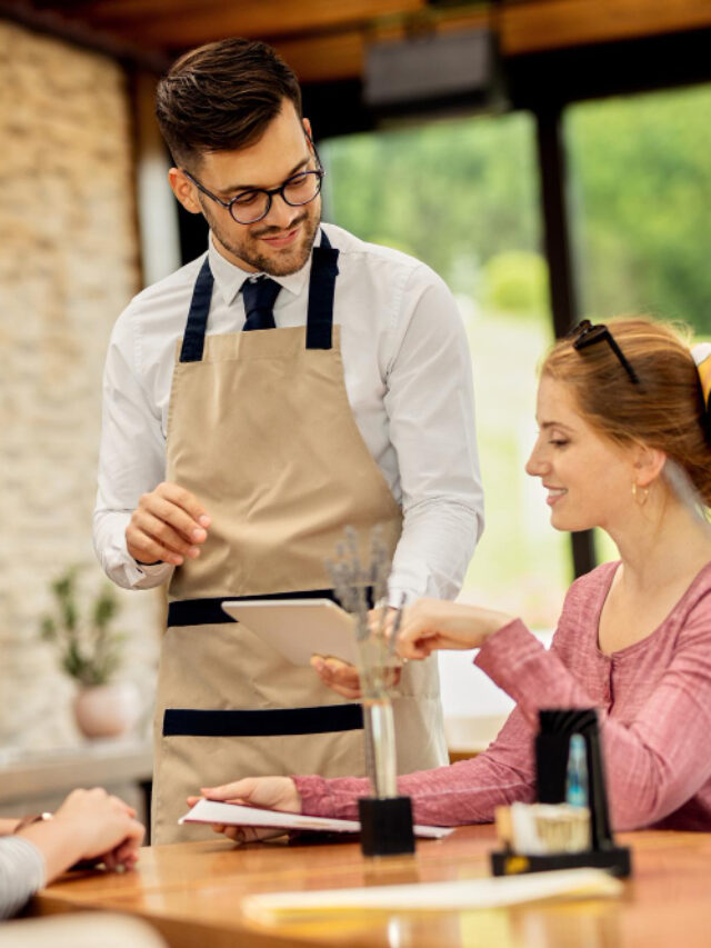 young-waiter-showing-menu-touchpad-his-customers-cafe