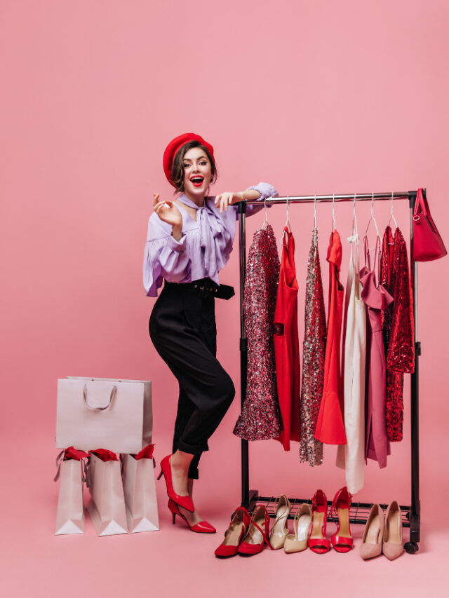 full-length-shot-elegant-lady-red-hat-black-purple-outfit-posing-with-hanger-with-elegant-dresses-shoes-packages