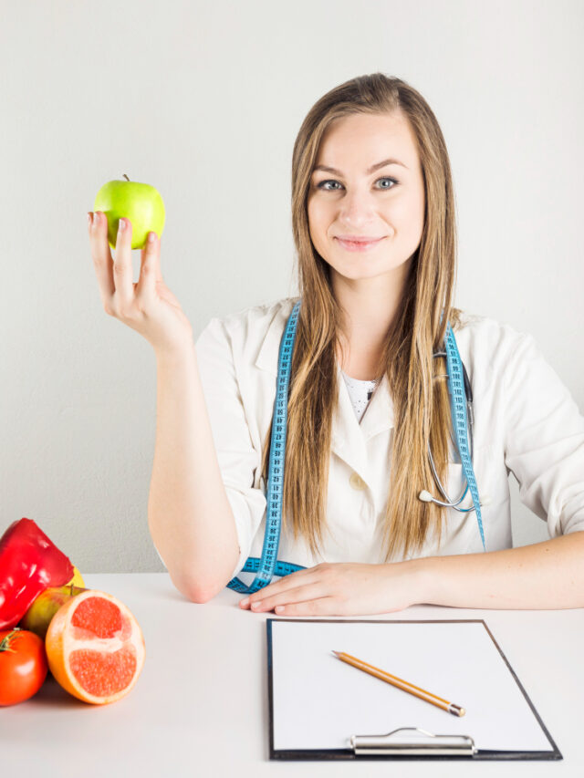 young-female-dietician-holding-green-apple-with-food-clipboard-desk